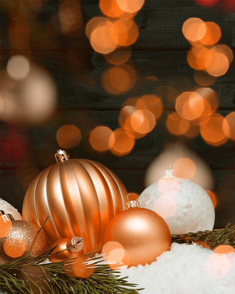 orange christmas ornaments on bed of snow with bokeh effect lighting in background